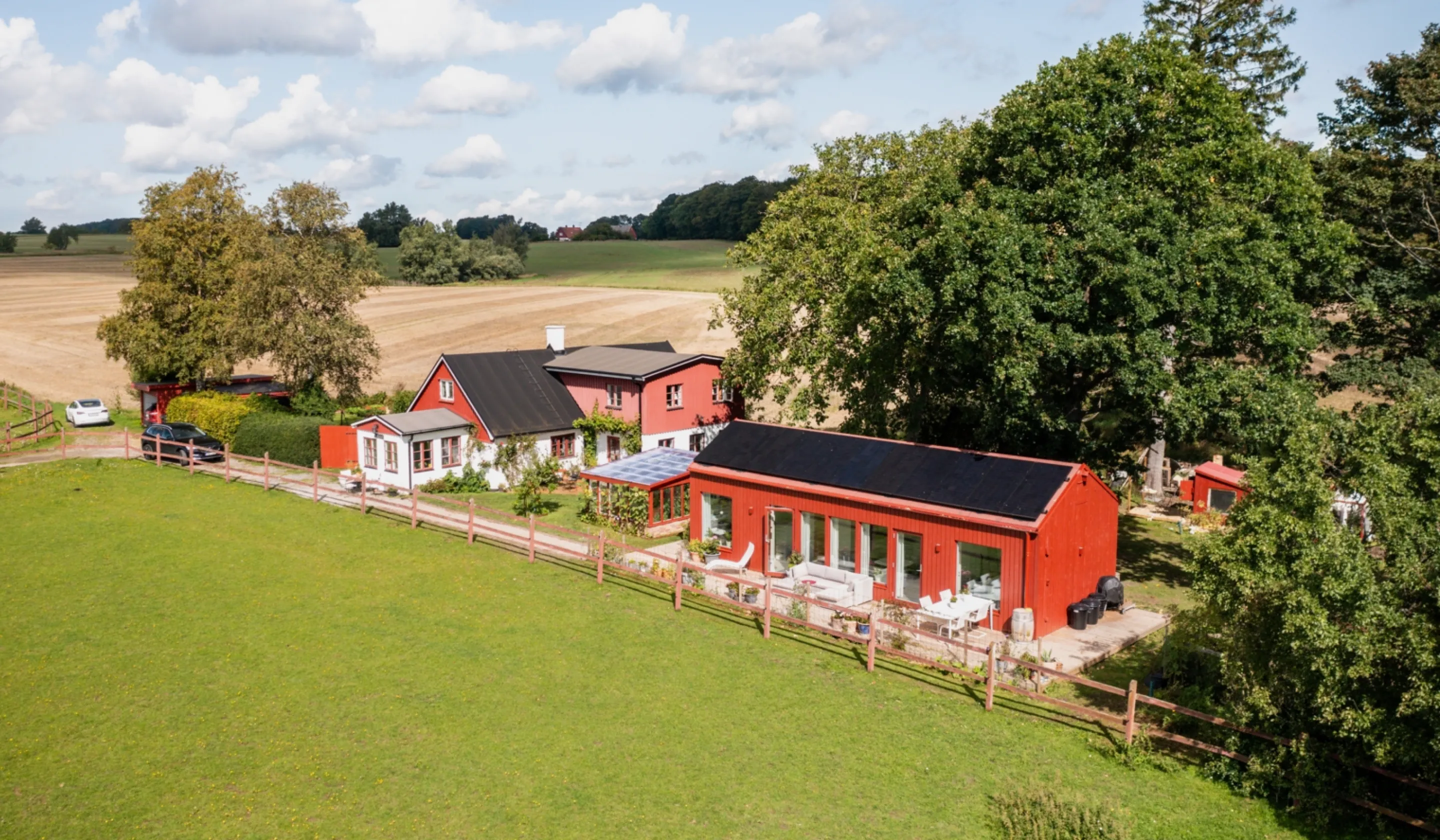 Röda och vita hus vid träd staket och åker
